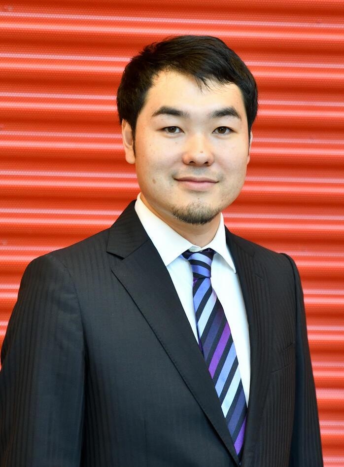 Young, male scientist in dark suit against a red, corrugated background